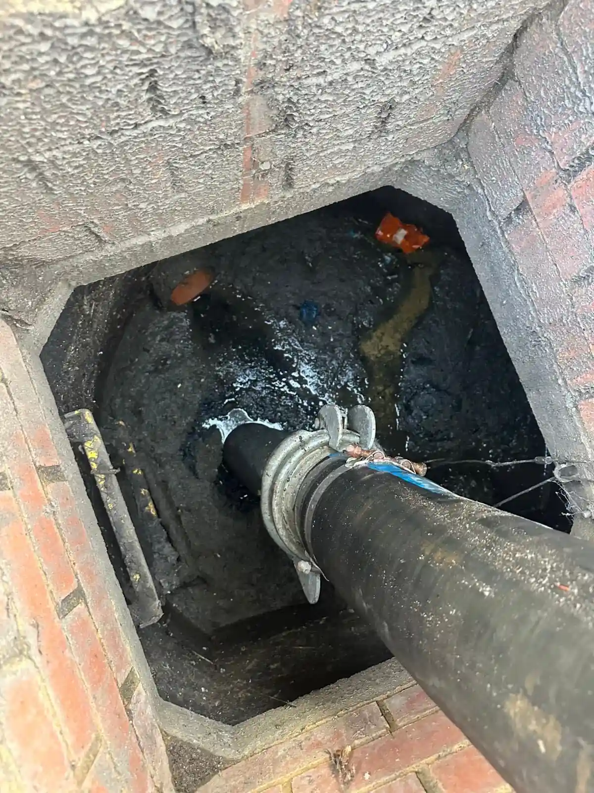 Jetting and suction hose clearing silt and debris from a brick drainage chamber at a commercial site in Berkshire